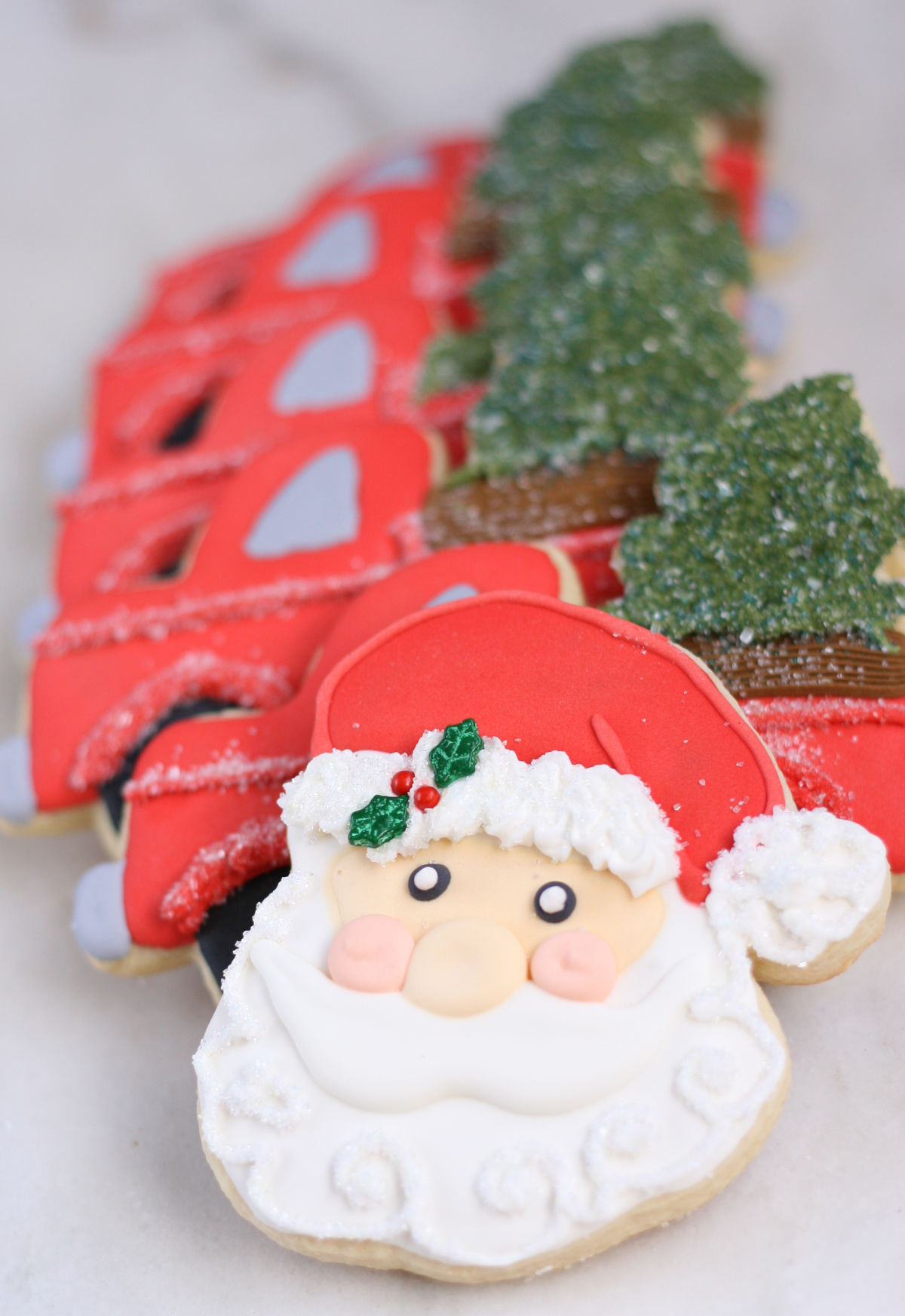 Decorated Santa sugar cookies on white marble, red truck cookies in background.