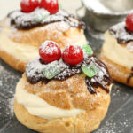 Cream puffs pastry cream and chocolate ganache, maraschino cherries and powdered sugar.