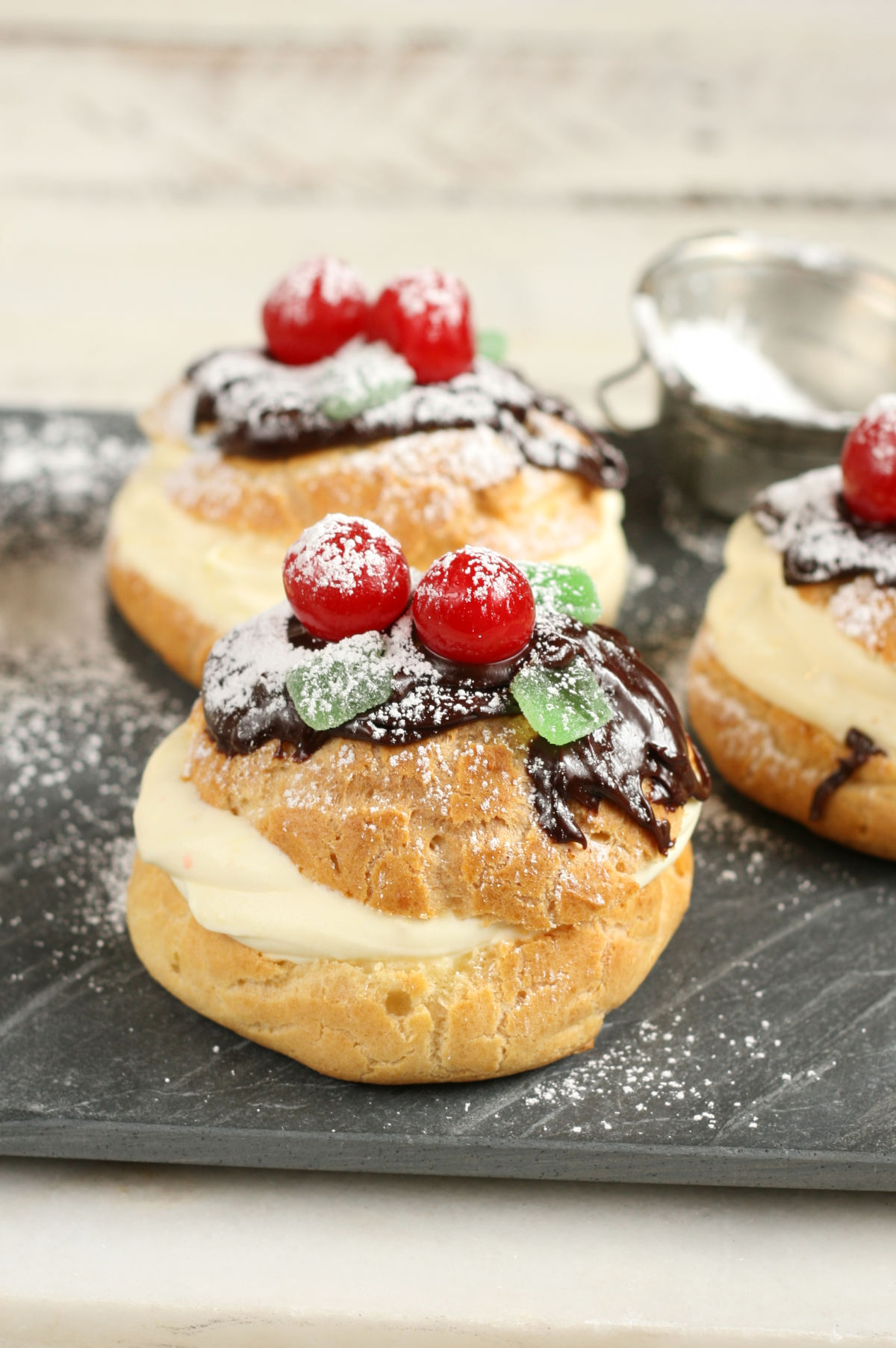 Cream puffs topped with chocolate ganache, maraschino cherries, mint candies, powdered sugar.