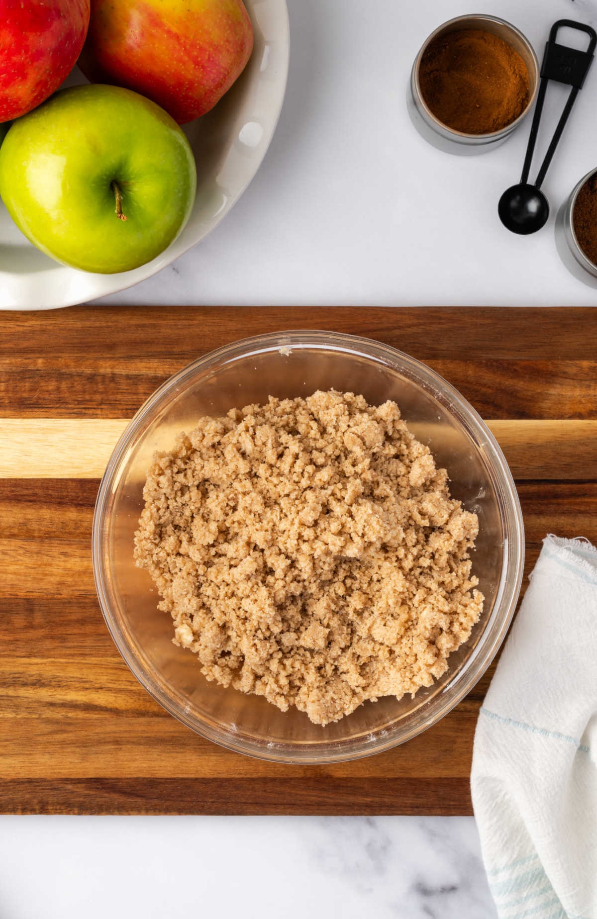 Crumb topping in clear glass bowl on wood cutting board.