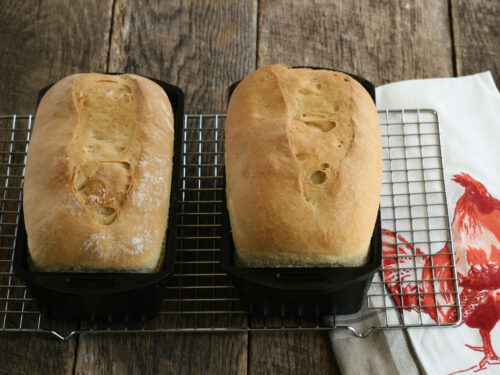 Two loaves of sourdough bread in cast iron loaf pans on metal baking rack.