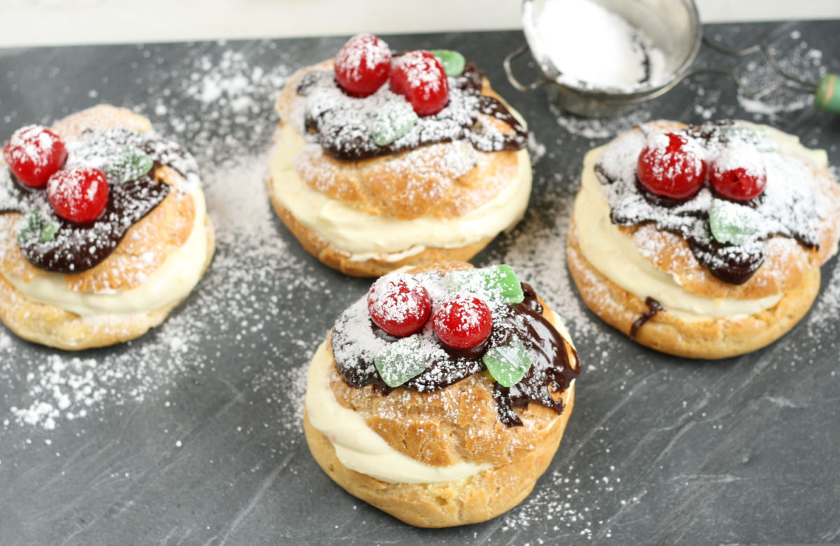 Four cream puffs with chocolate ganache, maraschino cherries and powdered sugar.