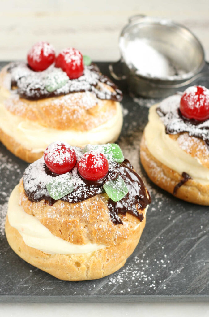 Cream puffs with pastry cream, chocolate ganache, maraschino cherries, green mint candies, powdered sugar.