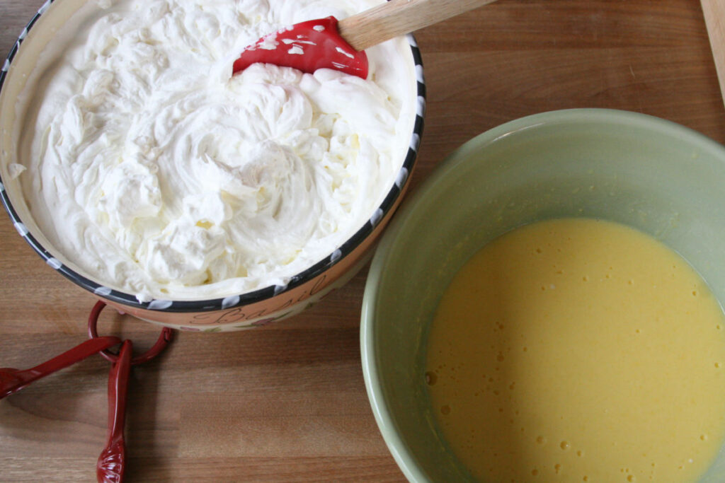 Two bowls, one with whipped cream, one with vanilla pudding on butcher block.