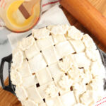 Unbaked pie with lattice crust and leaves on wooden cutting board, egg wash with pastry brush.