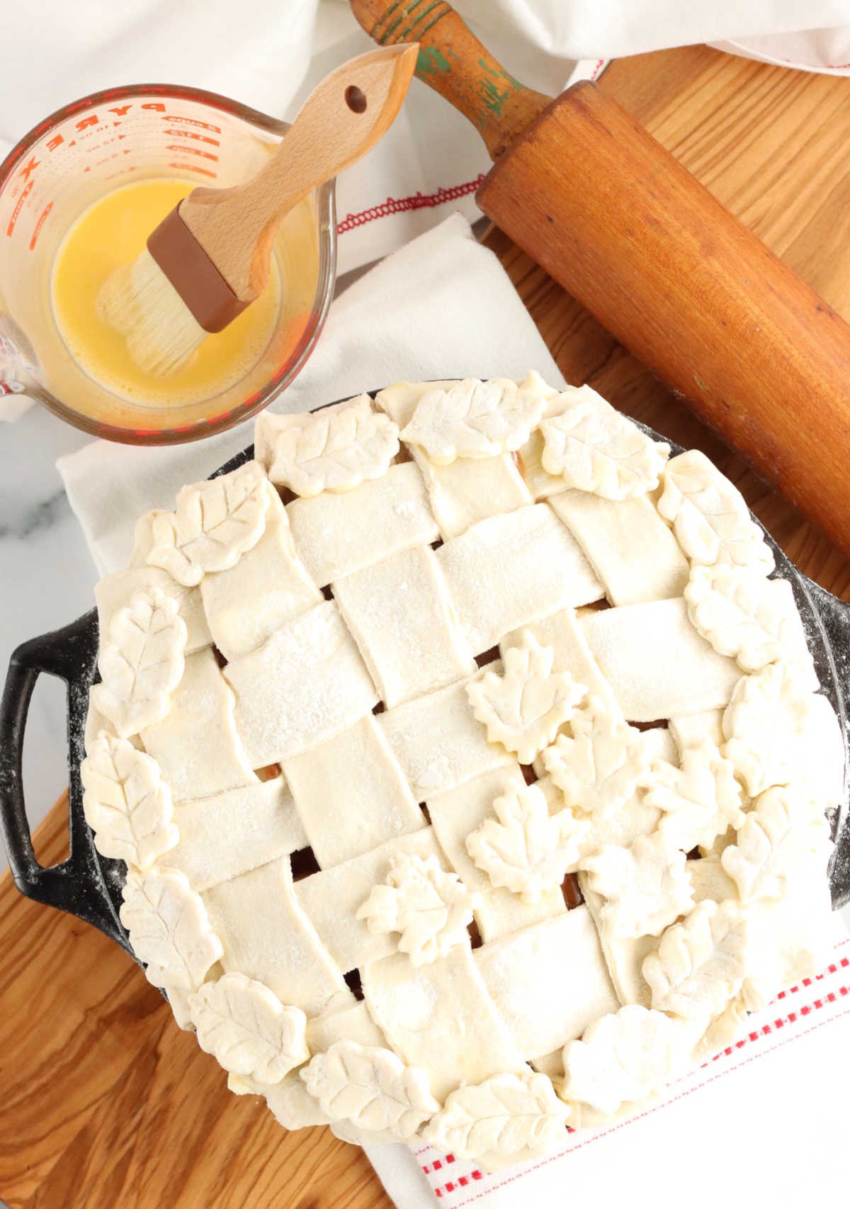 Unbaked pie with lattice crust and leaves in dual handle cast iron pie pan on wooden cutting board.