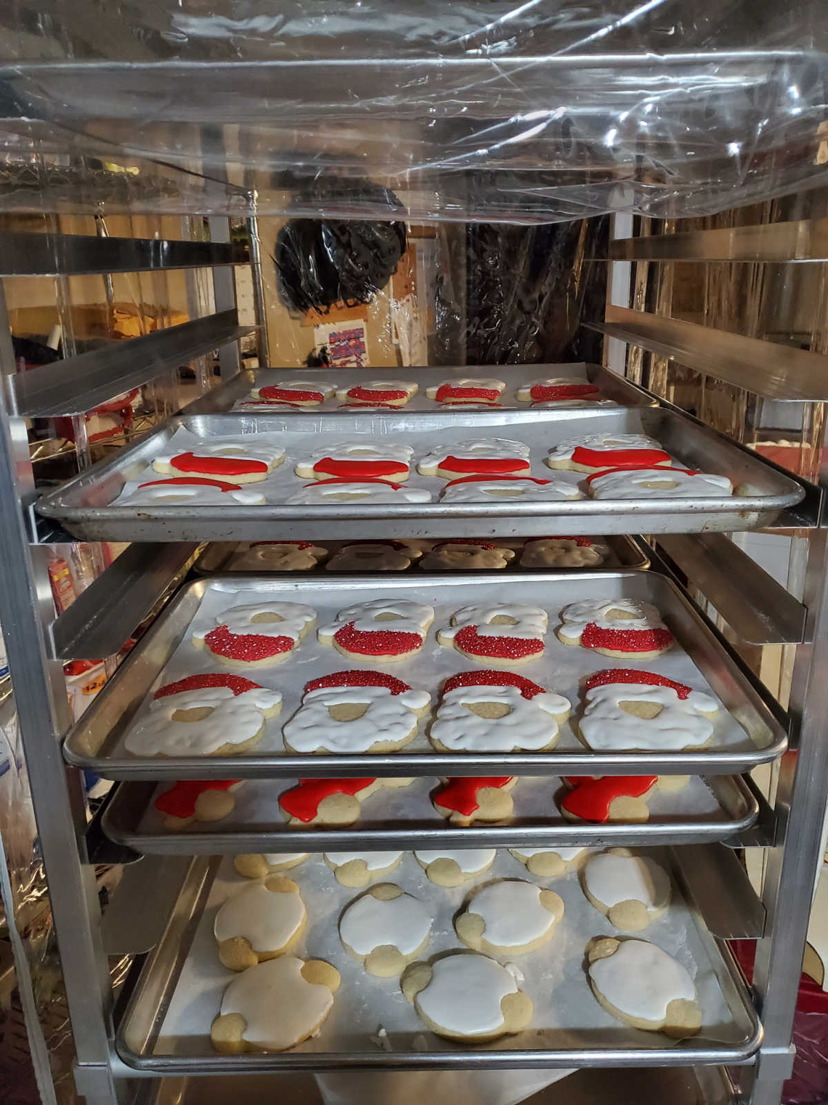 Baking rack with trays of Christmas cookies with icing drying.