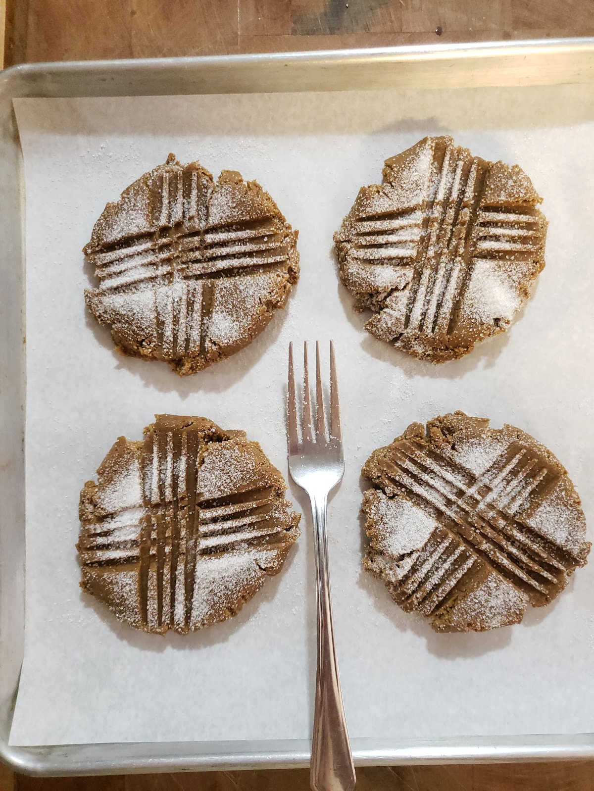 Unbaked molasses cookies with fork marks on sheet pan with parchment paper.