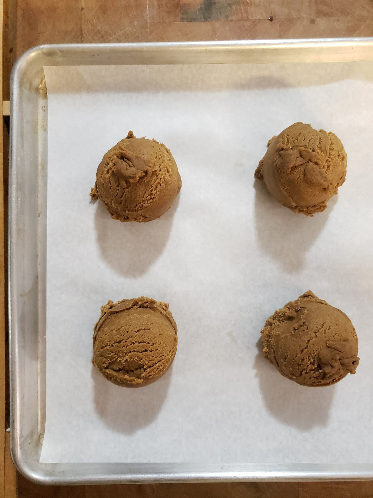Scooped molasses cookie dough on sheet pan with white parchment paper.