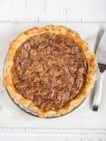 Pecan pie on white reclaimed wood, metal pie server to the right.