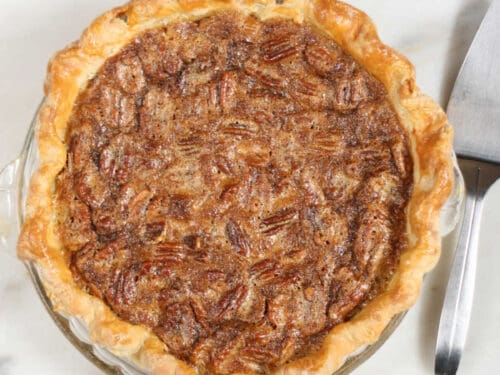 Pecan pie on white reclaimed wood, metal pie server to the right.