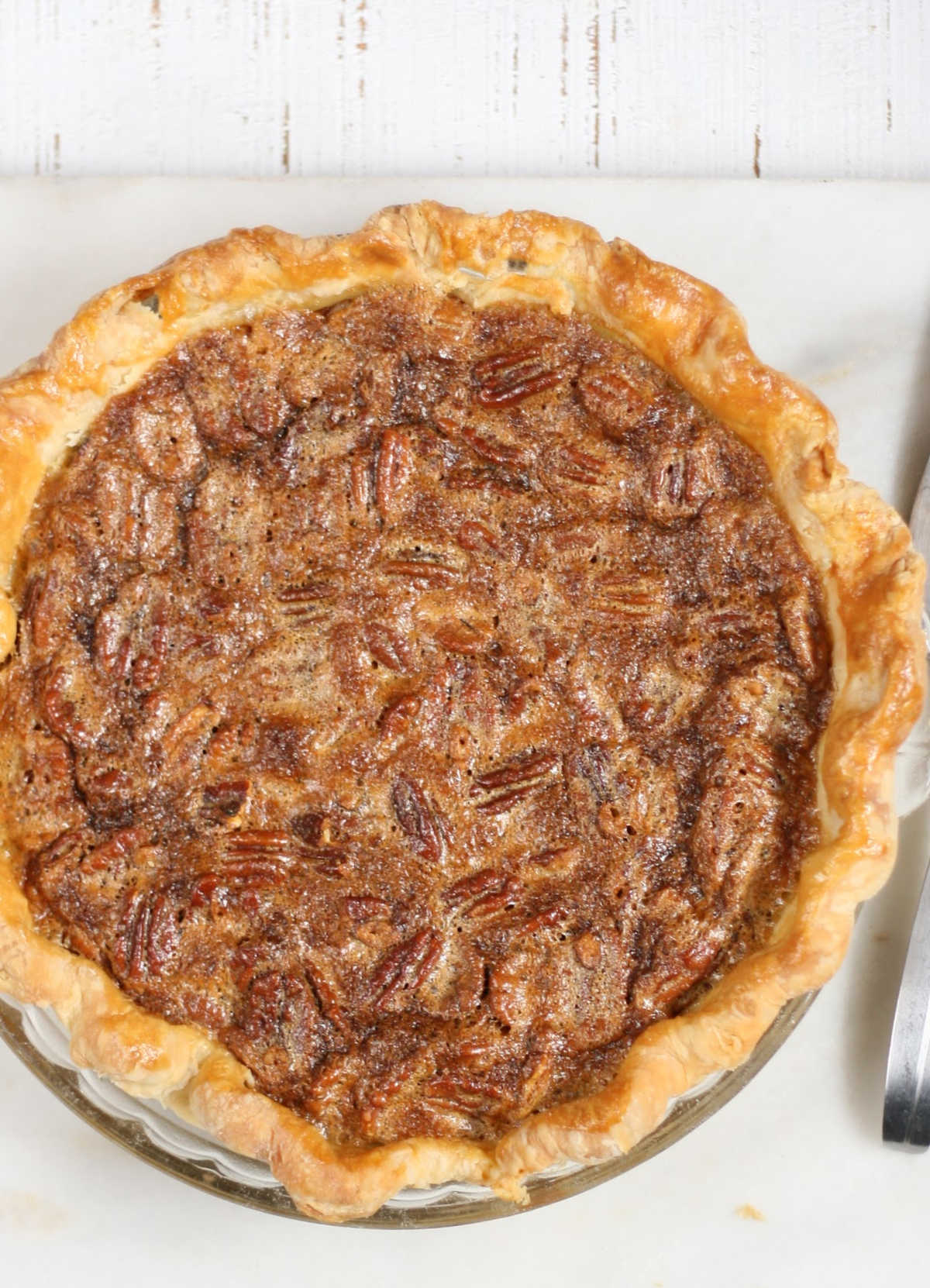 Close up of pecan pie with golden browned pie crust on white marble.