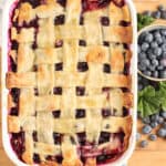 Blueberry cobbler with lattice pie crust in white rectangle baking dish on wooden cutting board.