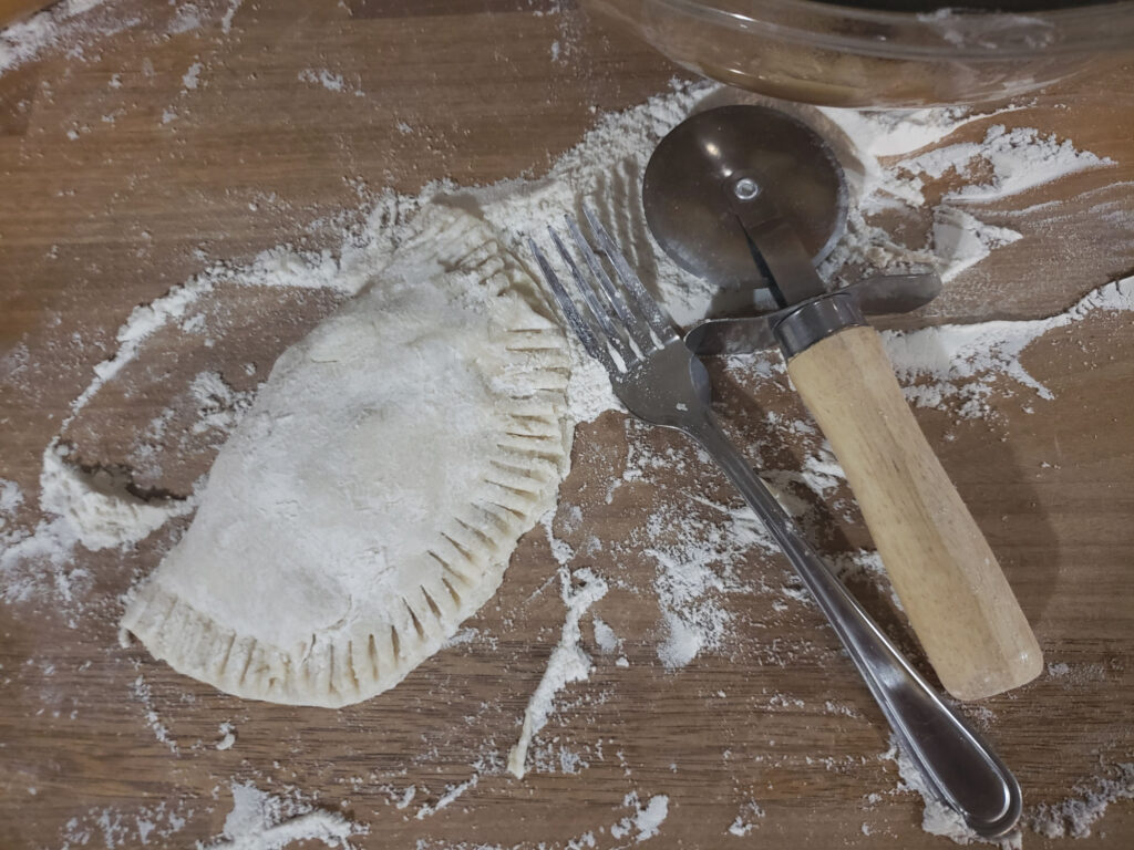 Hand pie being assembled on butcher block with fork and pastry wheel to right.