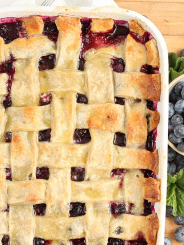 Blueberry cobbler with lattice pie crust, fresh blueberries around.
