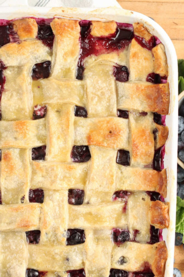 Blueberry cobbler with lattice pie crust, fresh blueberries around.