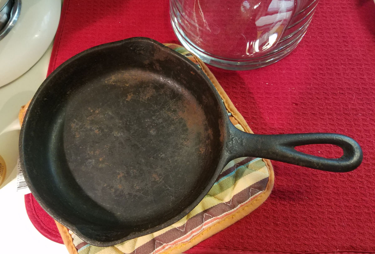 Cast iron skillet with rust before seasoning on kitchen counter.