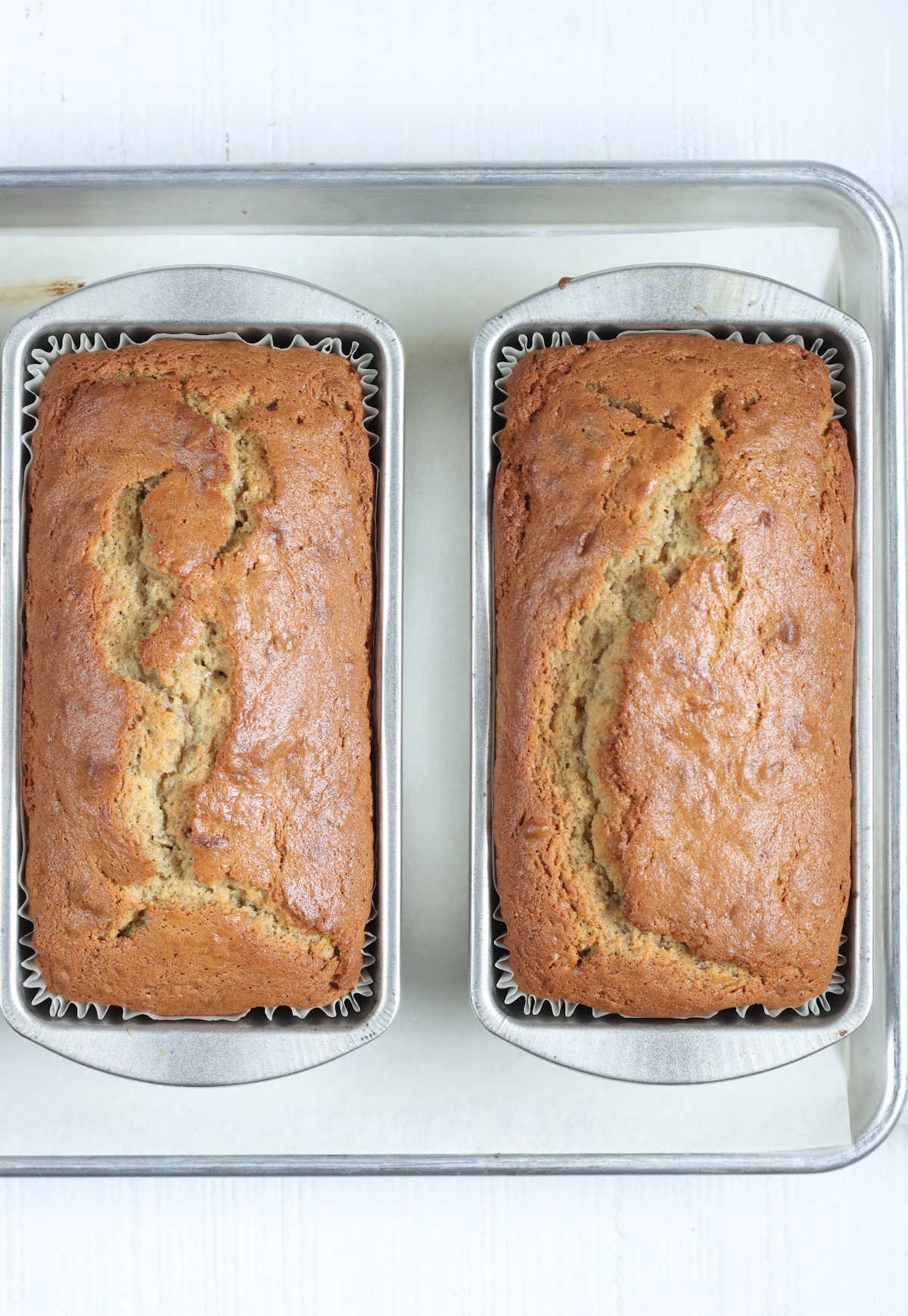 Two loaves of banana bread in metal loaf pans on sheet pan.