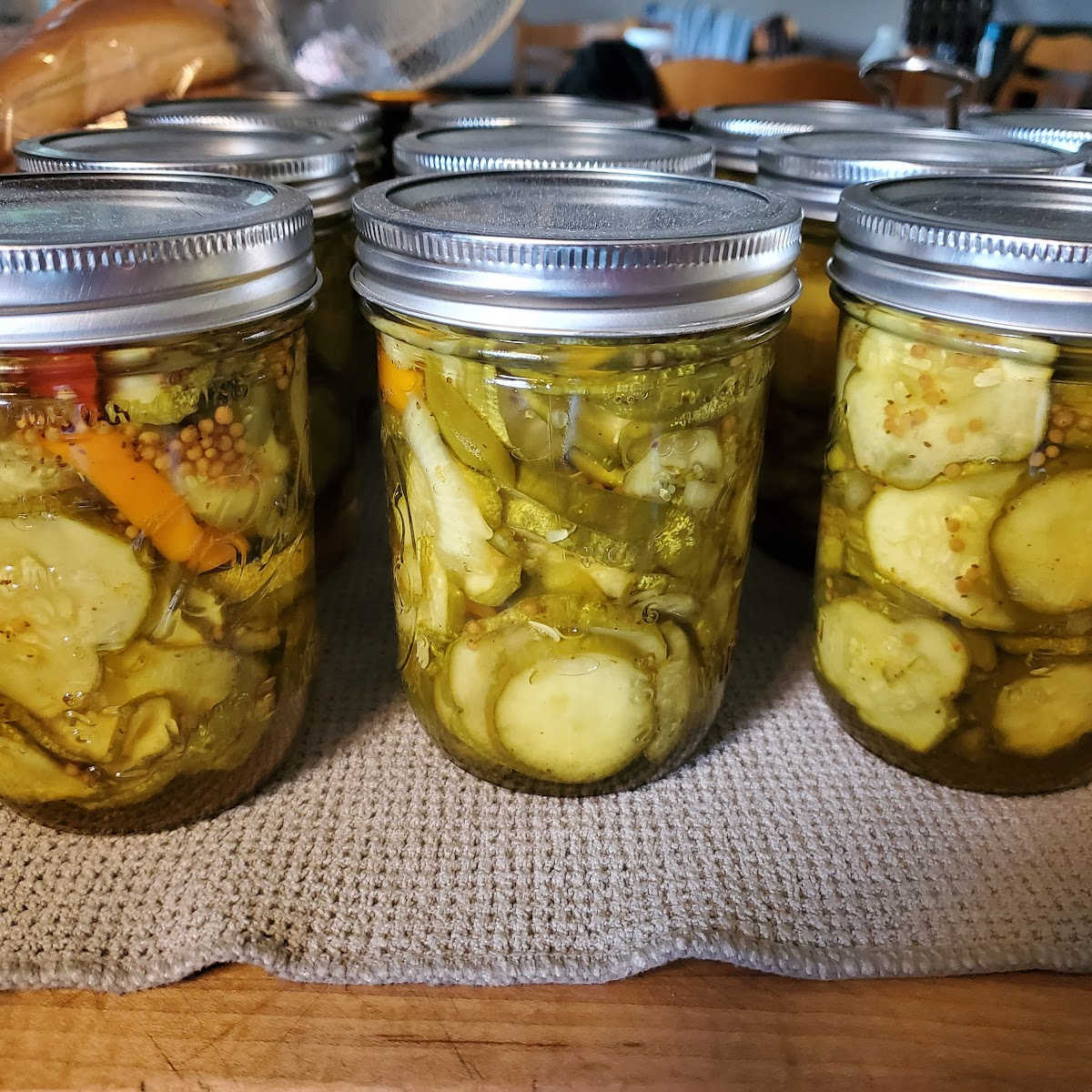 Wide mouth pint Mason jars with pickle slices cooling on wooden cutting board, taupe dish cloth under jars.