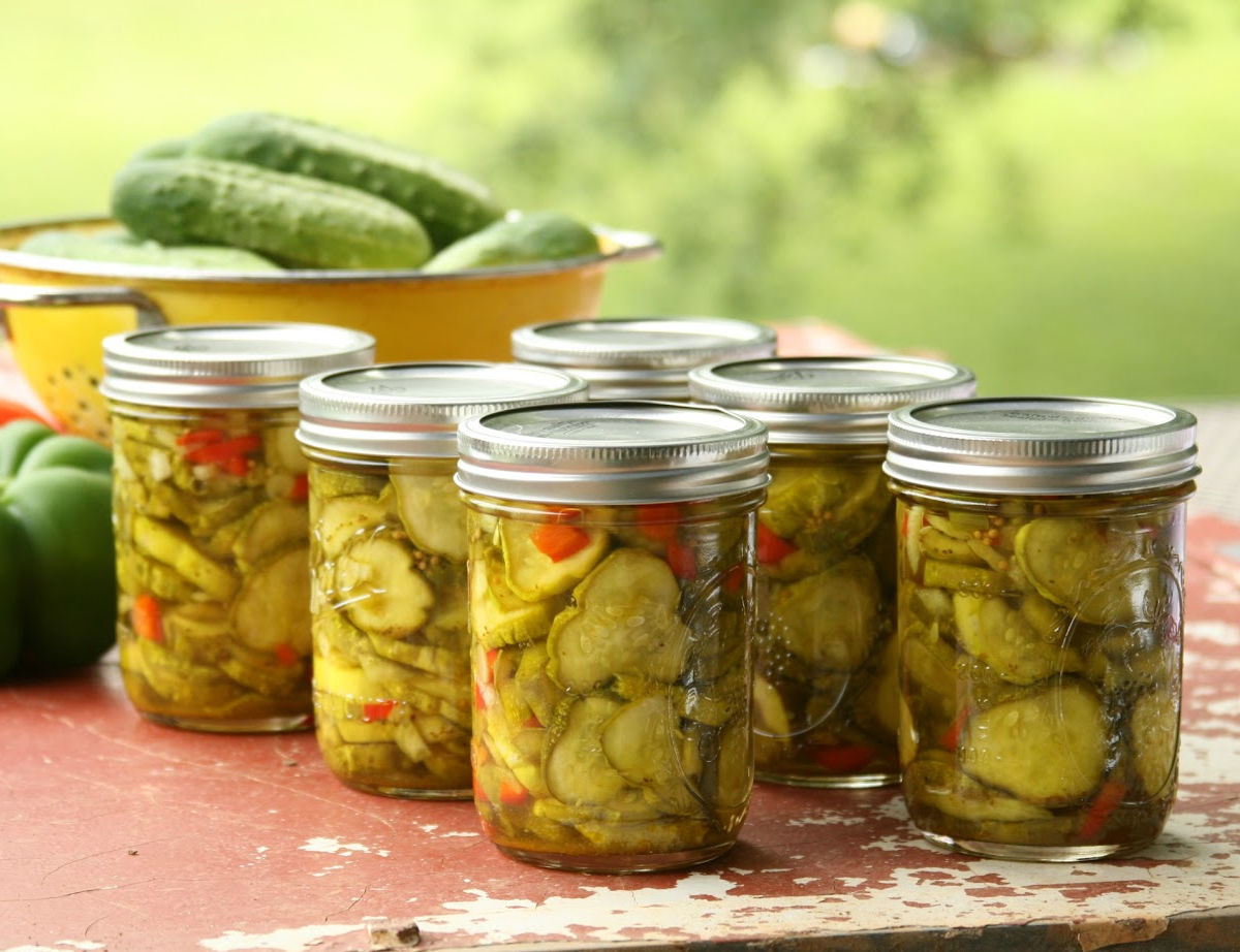 Mason jars of pickle slices on outdoor barn red patio table.