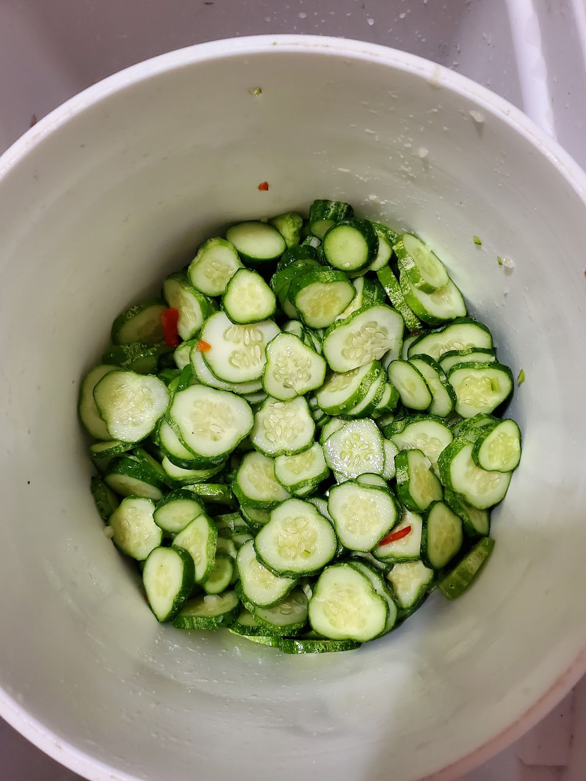 White 5-gallon bucket with sliced pickling cucumbers, red and green bell pepper slices, and yellow onion.