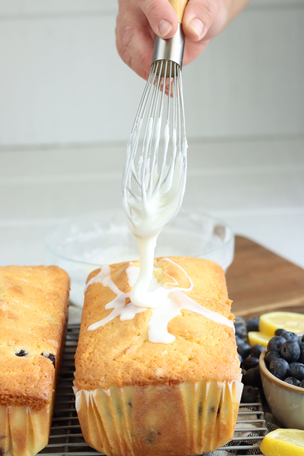 Hand holding whisk putting icing on lemon loaf cakes.