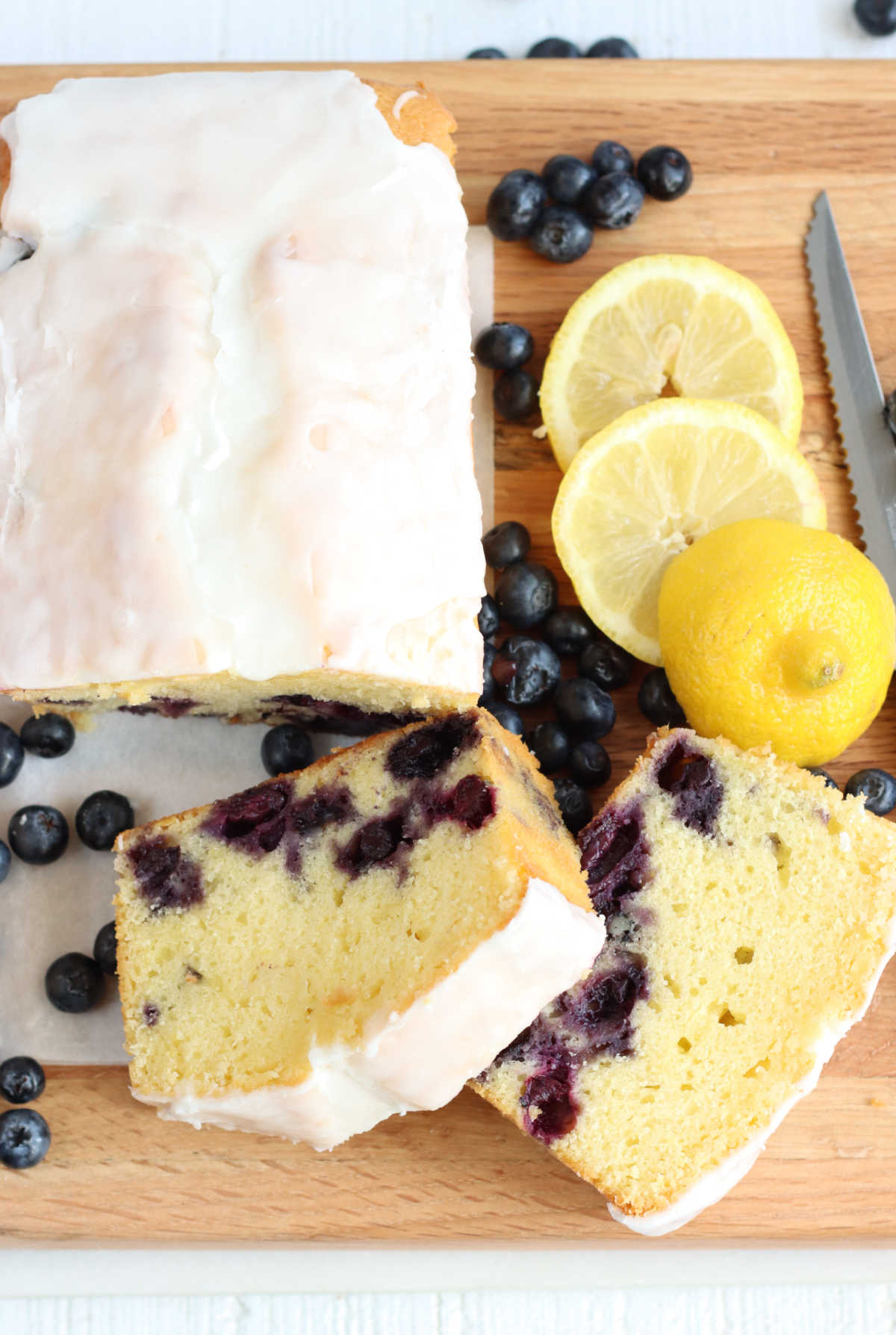 Lemon blueberry loaf cake partially sliced on wooden cutting board.