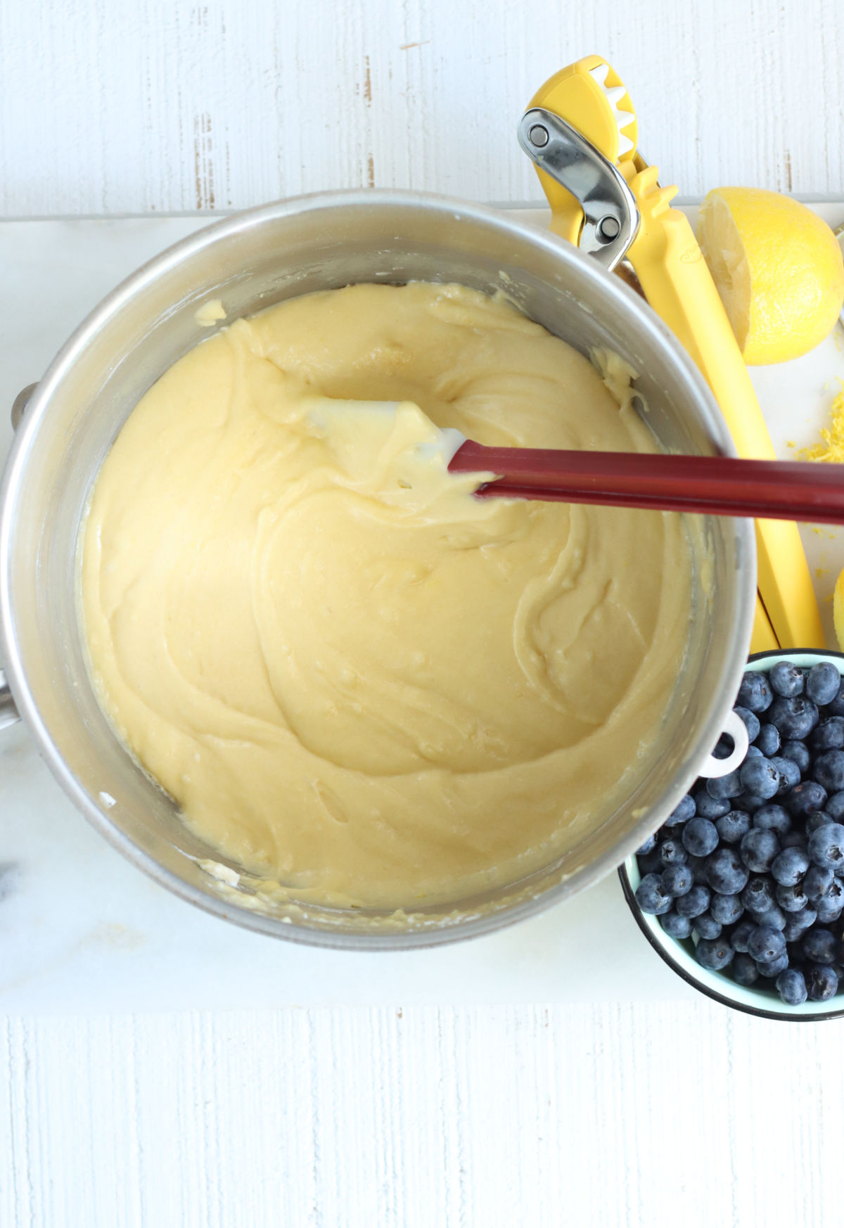 Lemon cake batter in metal mixing bowl, bowl of blueberries to right.
