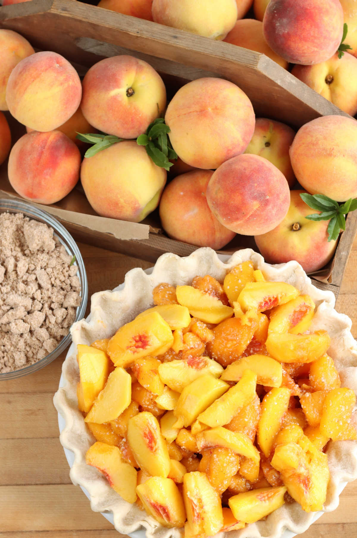 Peaches in wood box, peach slices in unbaked pie shell on butcher block.