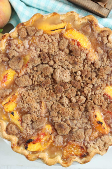 Peach crumb pie with peaches in background.