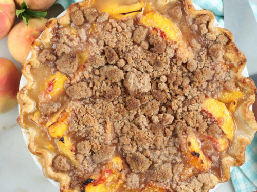 Peach crumb pie with peaches in background.