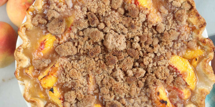 Peach crumb pie with peaches in background.