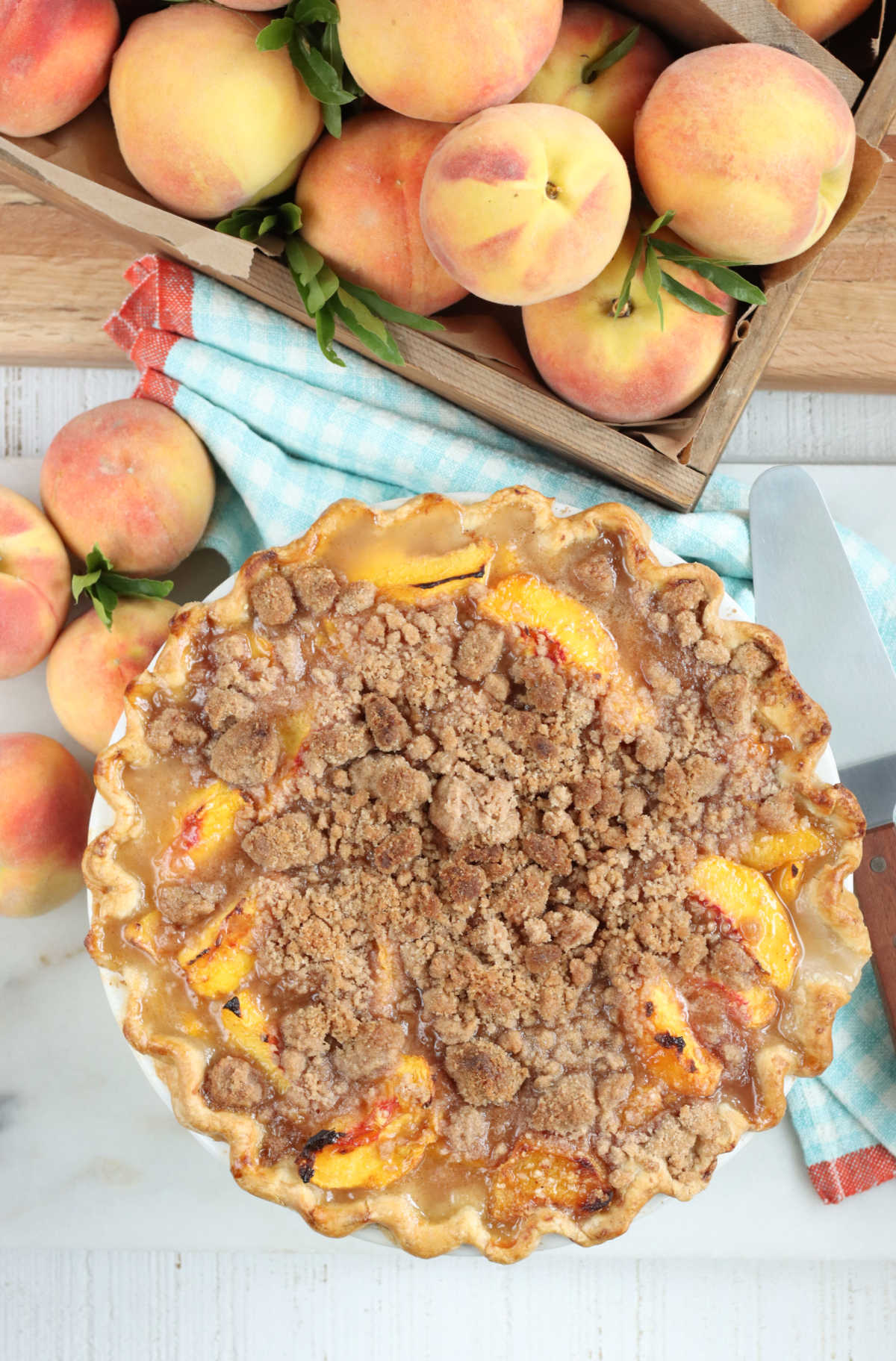 Peach pie with crumb topping, fresh peaches around in wooden box.