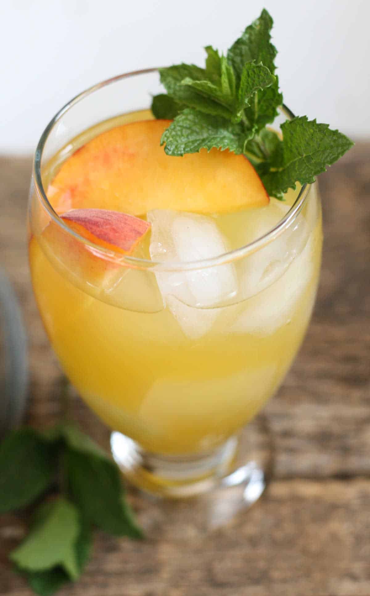 Summer sangria in clear footed glass with fresh peach slices, ice cubes, and a piece of fresh mint