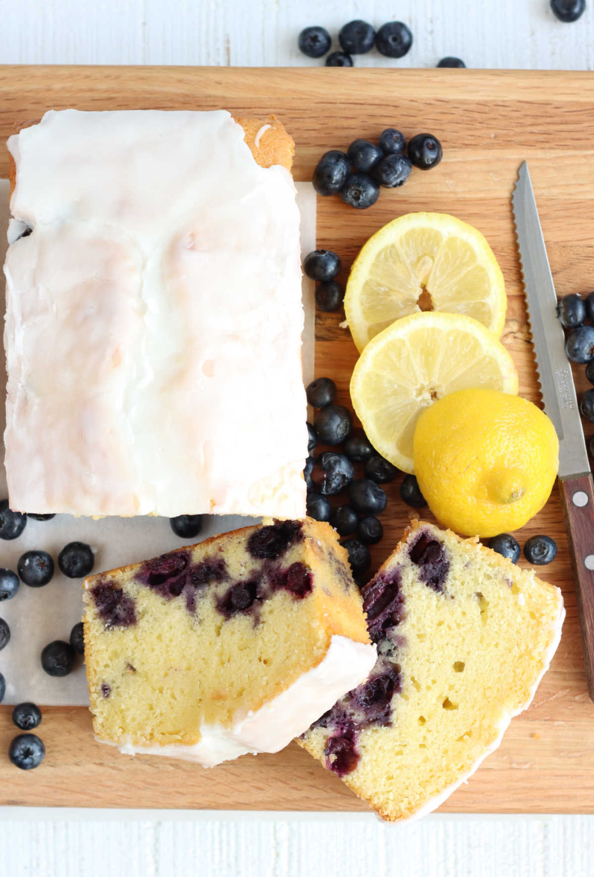 Lemon blueberry loaf cake sliced partially on wooden cutting board.