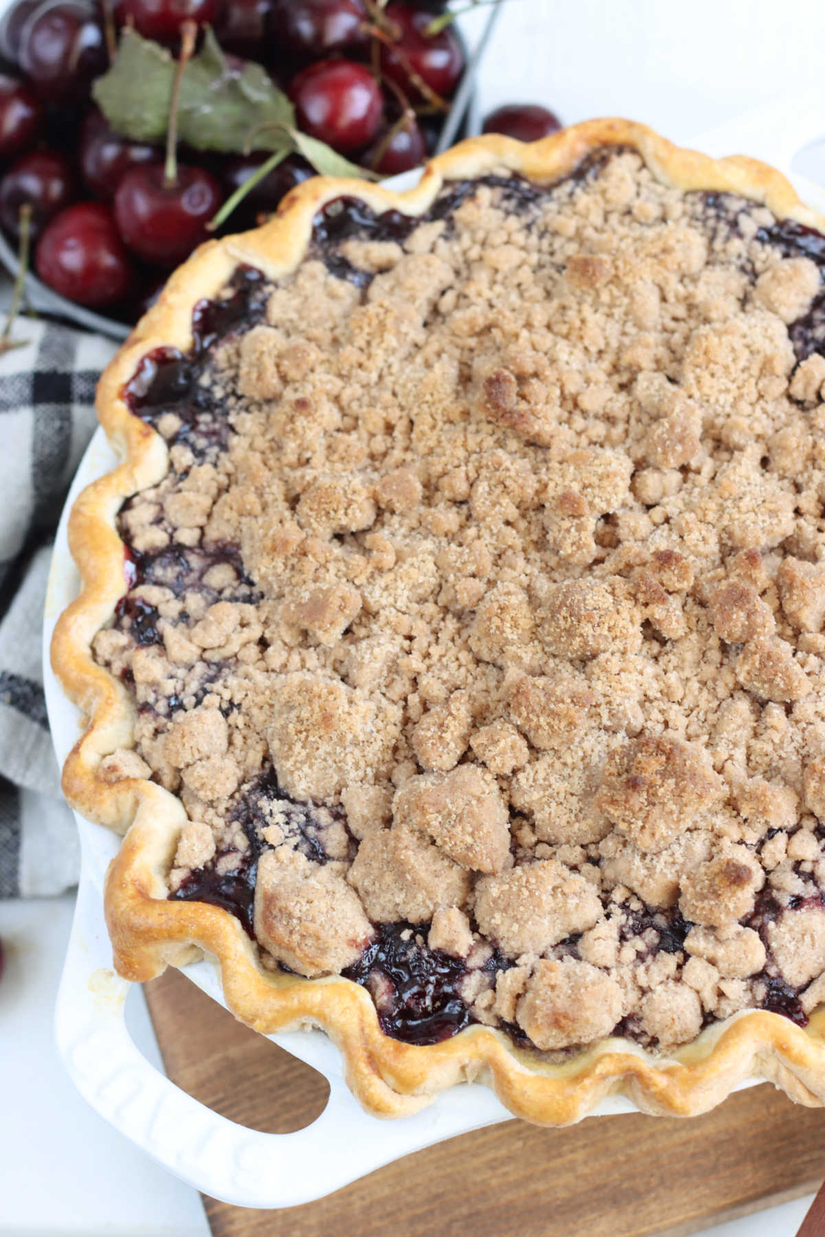 Close up of cherry crumb pie in white pie dish with dual handles.