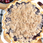 Cherry pie with crumb topping in dual handle white pie pan.