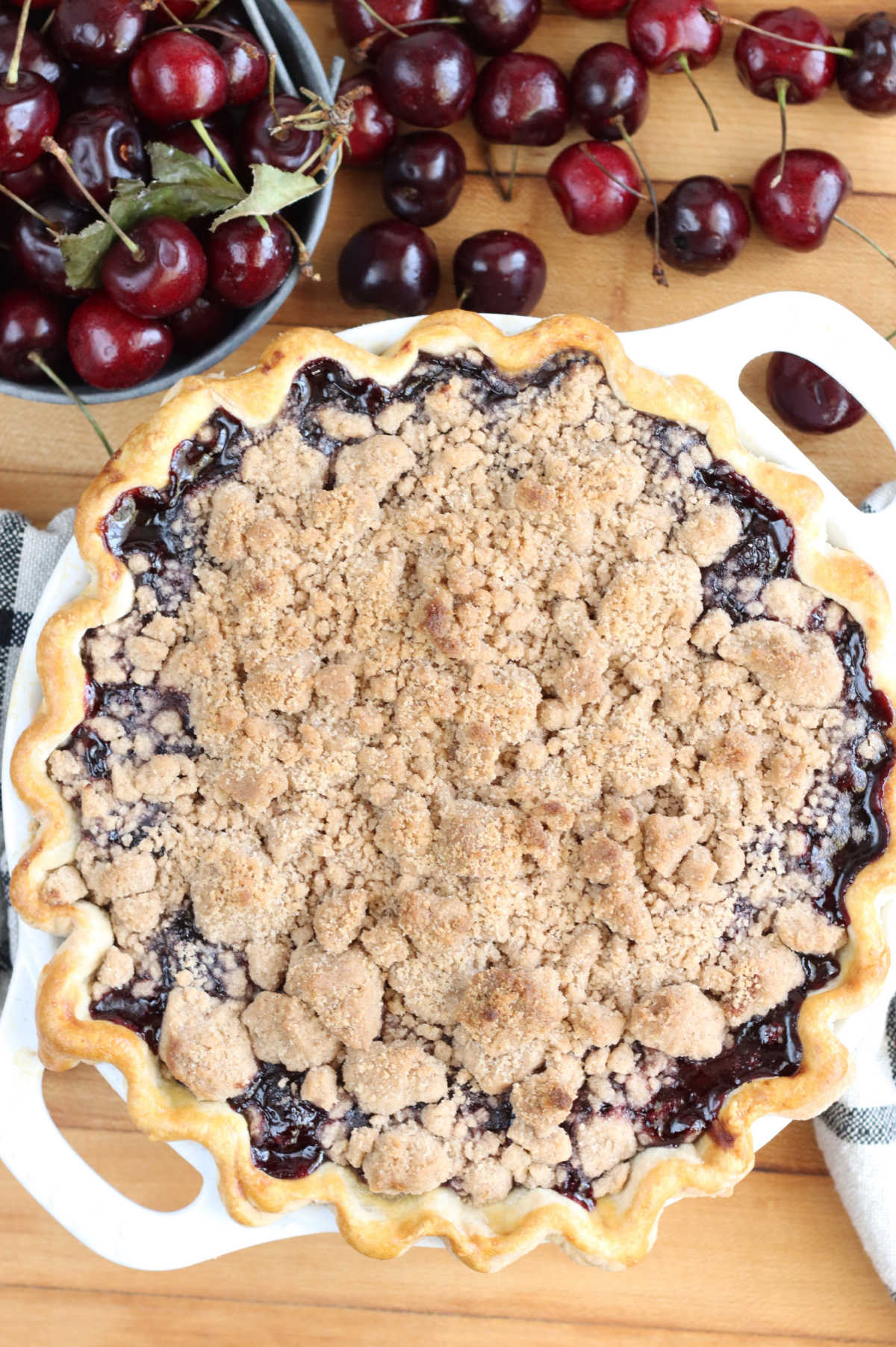 Cherry pie crumb topping in dual handle white pie dish on wooden cutting board.