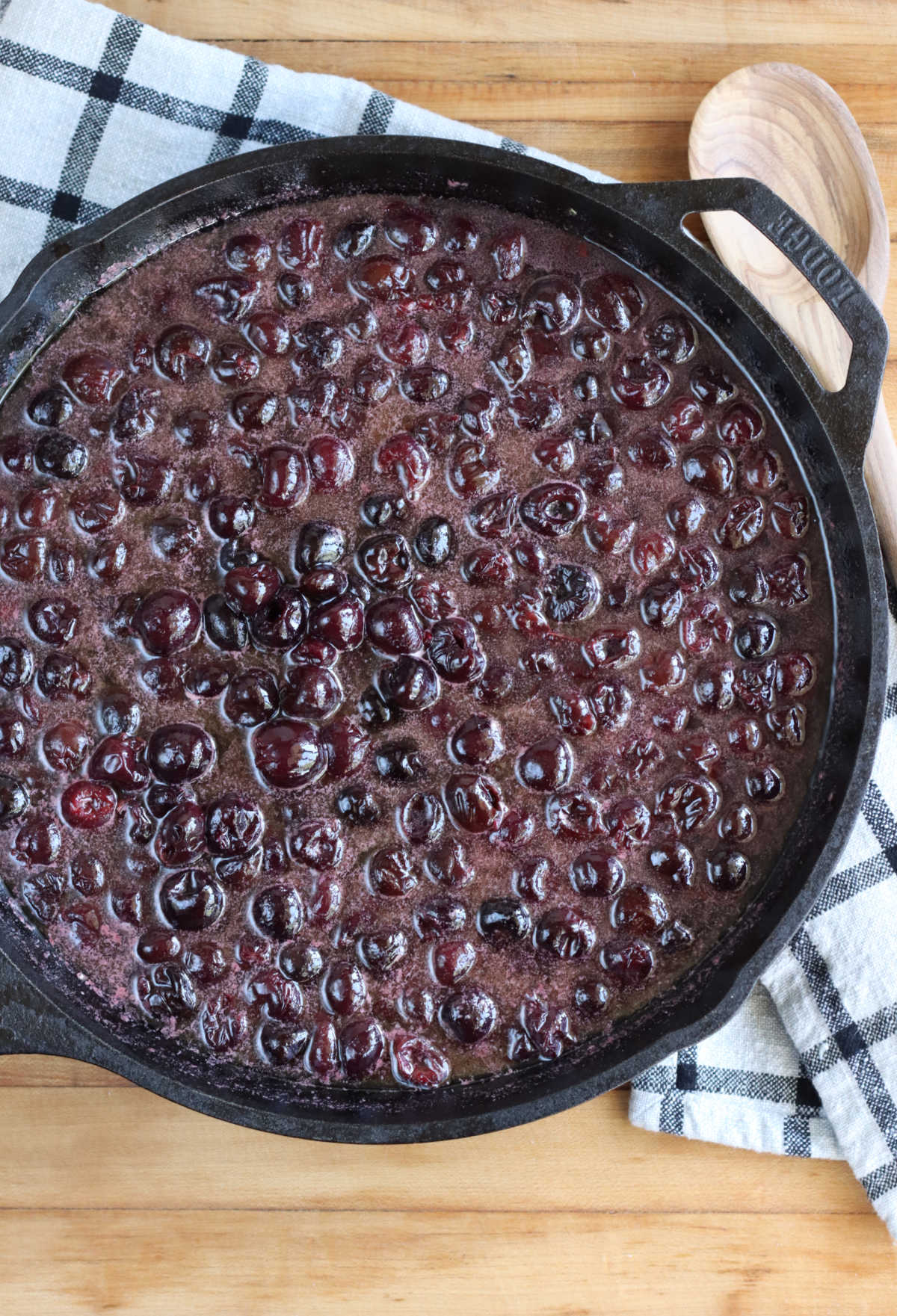 Cherry pie filling in large cast iron skillet on wooden cutting board,
