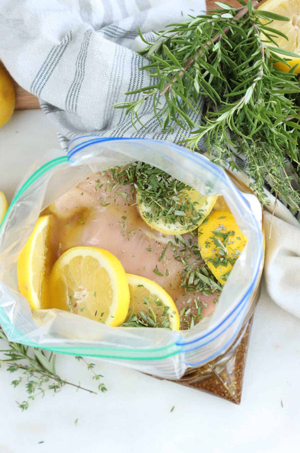 Large zip-style bag with chicken breasts marinating, lemon slices and herbs.