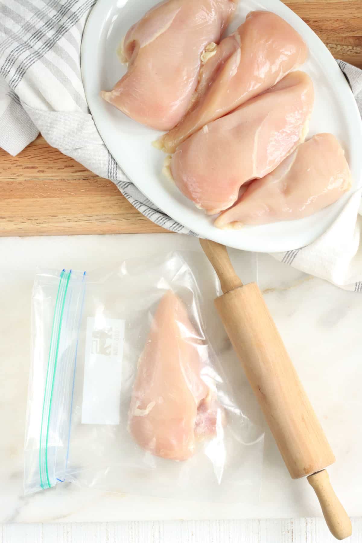 Chicken breasts on white plate, chicken breast in zip-style bag with small rolling pin on white marble.
