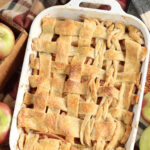 Cobbler with lattice pie crust in white baking dish, apples around.