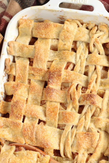 Cobbler with lattice pie crust in white baking dish, apples around.