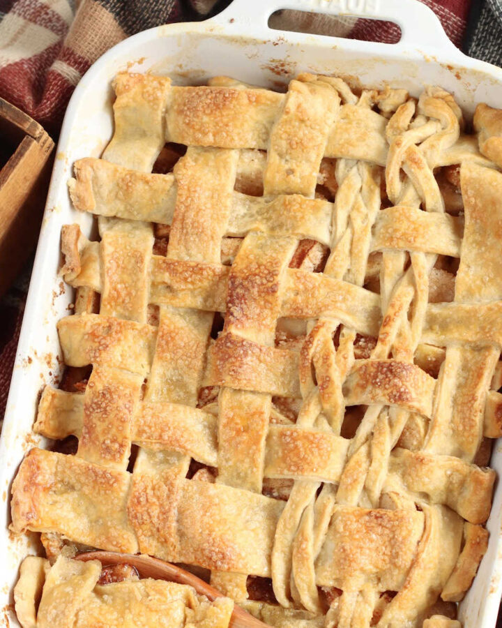 Cobbler with lattice pie crust in white baking dish, apples around.