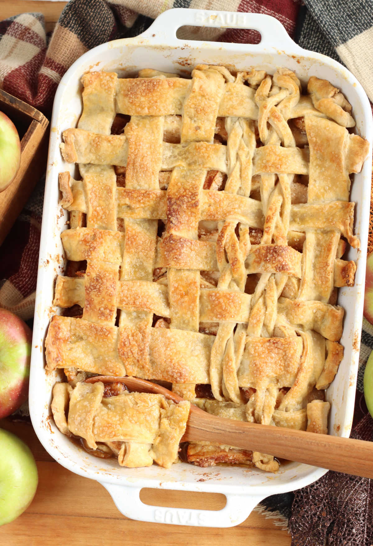 Cobbler with apples and pie crust in white baking dish on wood cutting board.