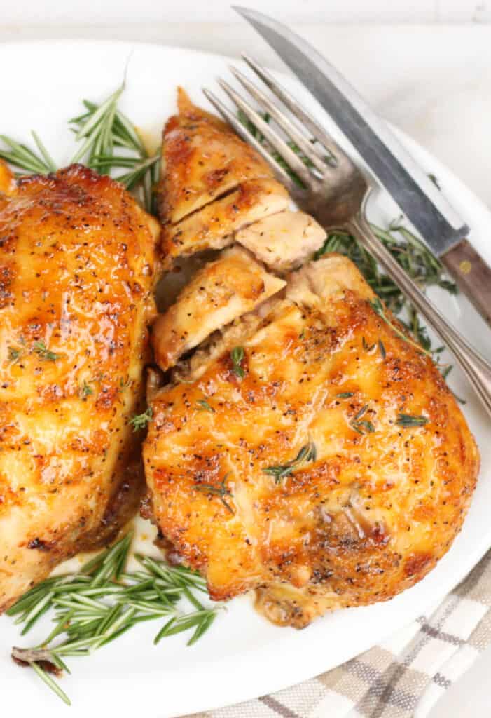 half breasts of chicken on a white serving plate with slices of oranges.