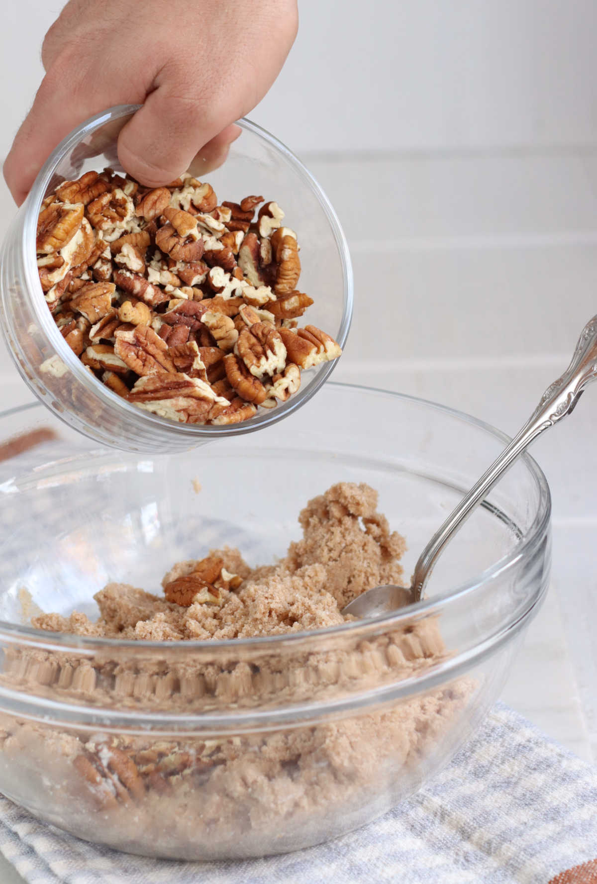 Dumping pecans into crumb topping in clear glass bowl.