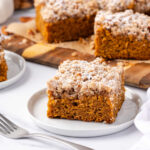 Square of pumpkin crumb cake on small white plate with fork.