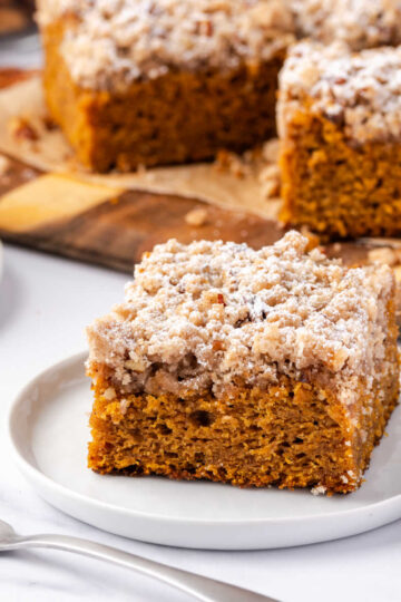 Square of pumpkin crumb cake on small white plate with fork.