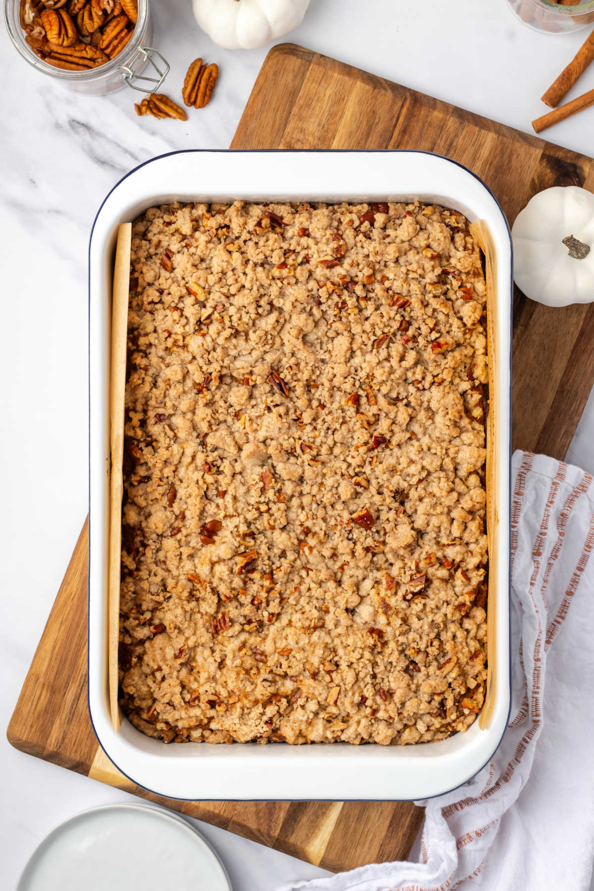 White cake pan with crumb cake on wood cutting board.
